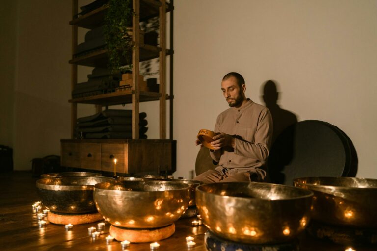 A man sitting indoors with Tibetan singing bowls and candles, creating a peaceful ambiance.
