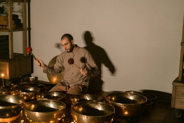 A man using Tibetan singing bowls for healing and relaxation in a serene indoor setting.