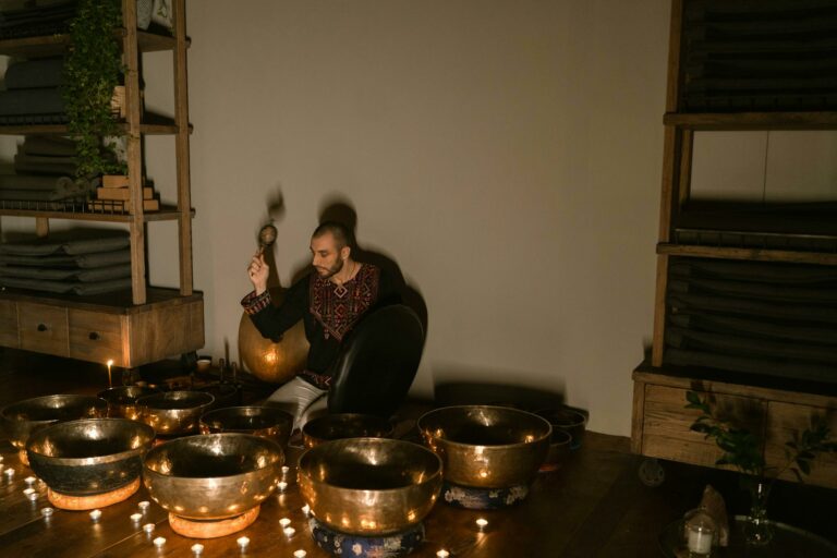 A serene indoor setting with a man playing Tibetan singing bowls surrounded by candles, promoting relaxation and mindfulness.